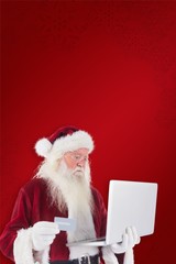 Composite image of santa pays with credit card on a laptop