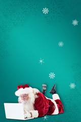 Composite image of santa lies in front of his laptop