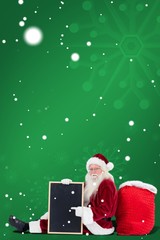 Composite image of santa sits leaned on his bag with a board