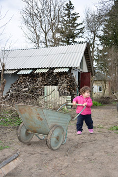 In the spring of small rural girl carries a wheelbarrow.