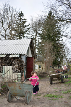 Spring dirty little village girl carries a wheelbarrow.