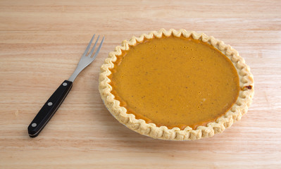 Freshly baked pumpkin pie with fork to the side on a table