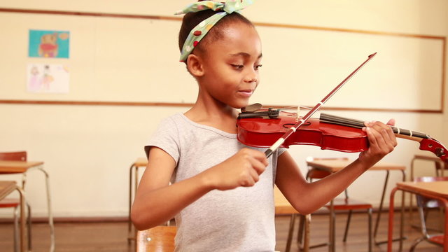 Cute pupil playing violin in classroom