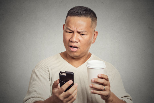 Worried man reading news on smartphone drinking coffee
