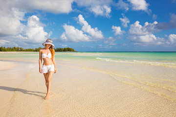 Fototapeta premium smiling woman in white shirts and hat walking on beach