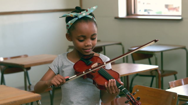 Cute pupil playing violin in classroom