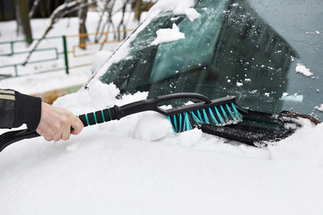 Man cleans car from snow with brush