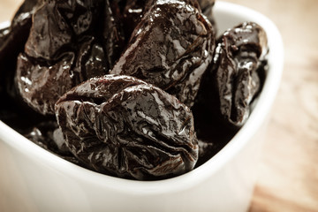 dried plums prunes in white bowl on wooden table