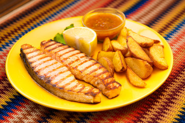 Grilled salmon steak with potatoes and sauce on a yellow plate