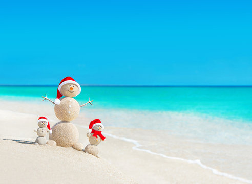 Snowmen family at tropical beach in santa hats. New Years and Ch