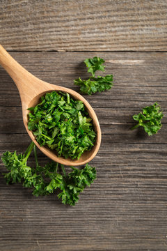 Fresh parsley flakes on spoon. On wooden board. 