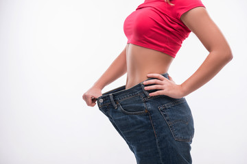 Slim waist of young woman in big jeans showing successful weight