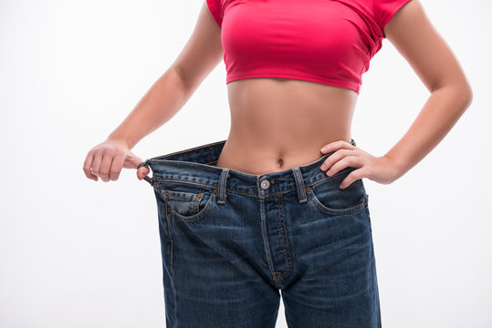 Slim waist of young woman in big jeans showing successful weight
