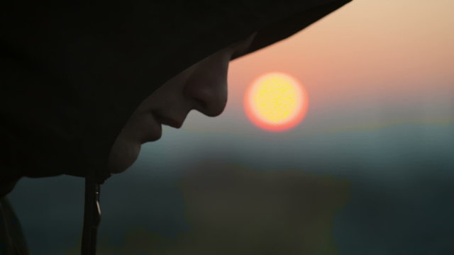 Sad young man in the hood at sunset