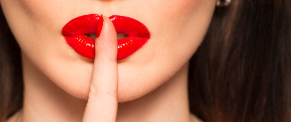 Naklejka premium makro ust z czerwonym palcem szminki pokazujący ciszy i ciszy