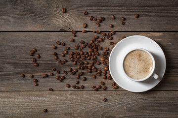 Coffee mug with roasted coffee beans on wooden table.