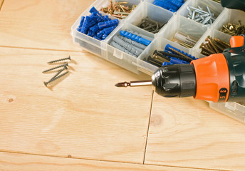 cordless drill, screws and toolbox on a wood background