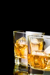 whiskey with ice in glasses on black background