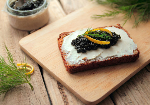 Tasty dark bread with black caviar on wooden board