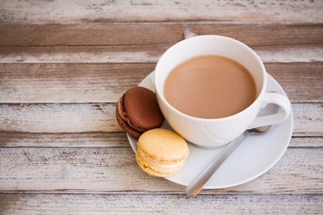 Cup of coffee with milk and macarons on wooden table