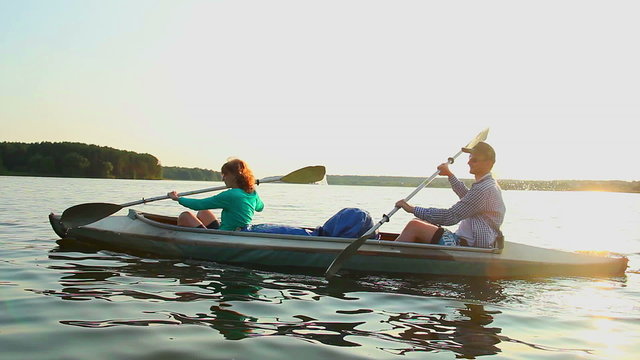 Young positive couple paddling kayak at sunset, beautiful view