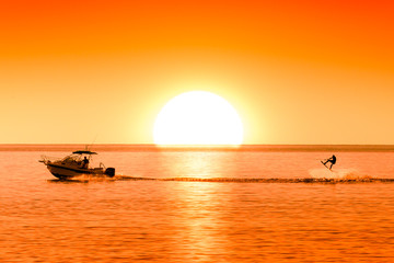 silhouette of boat and wakeboarder at sunset