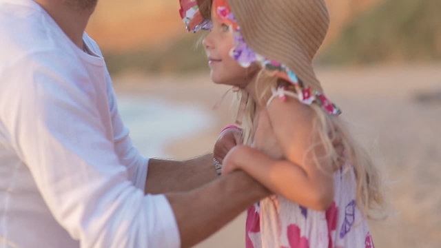 Father picks up little girl in hat on sea in slow motion