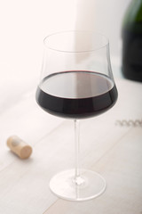 A glass of red wine with cork and bottle on table
