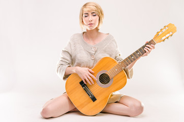 Fototapeta premium Young beautiful smiling blonde lady in sweater playing guitar