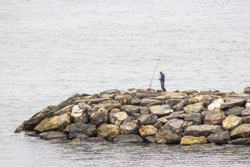 Fisher man with fishing rod on the stone groyne