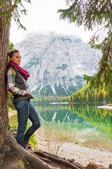 Naklejka premium Young woman standing near tree on lake braies in south tyrol