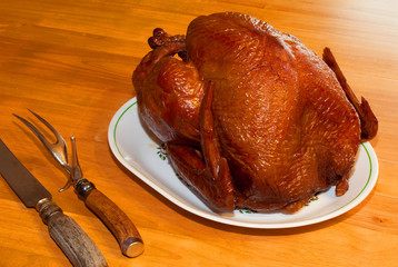 Holiday meal of a smoke turkey, seen on a plate with carving knife and fork at the side