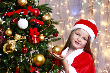 Little girl near Christmas tree on bright background