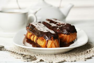 Tasty eclairs and cup of tea on wooden table