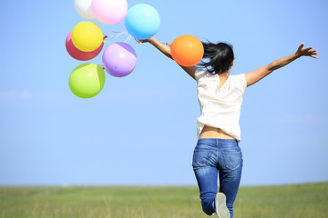 Fototapeta na wymiar young asian woman on green grassland with colored balloons 