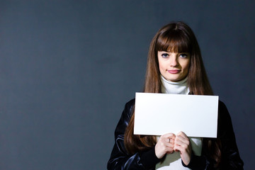 Young women holding empty white blank card on a dark wall backgr