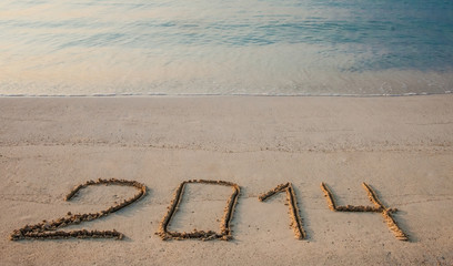 Tranquil morning seashore with 2014 drawn on sand