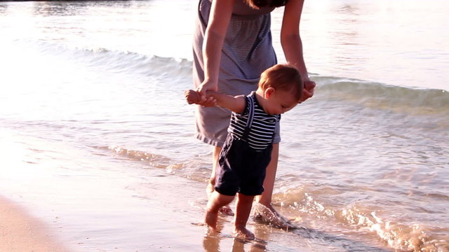 Mother helping his little son making first steps on the beach