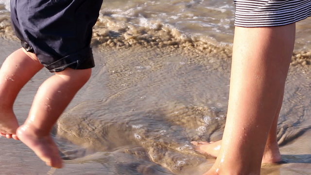 Mother helping his little son making first steps on the beach