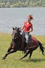 Cowgirl galloping bay horse on riverside
