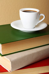 Pile of books with cup on tabletop and light wall background
