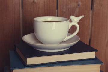 Pile of books with cup on tabletop and wooden background