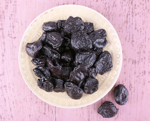 Plate with heap of prunes on color wooden background