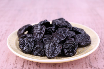 Plate with heap of prunes on color wooden background