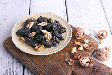Wooden board with plate of prunes and walnuts