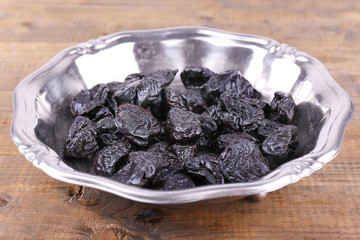 Metal plate of prunes on wooden background