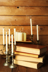 Retro candlesticks with candles and books, on wooden background