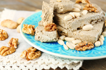 Sunflower halva with nuts on plate, on wooden background