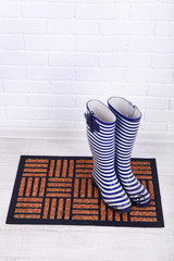 Naklejka premium Dirty wellington boots on door mat in room