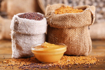 Mustard seeds in bags and sauce in bowl on  wooden background